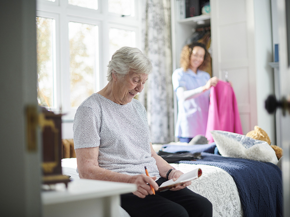 home carer helping assisted living senior woman get dressed in her bedroom